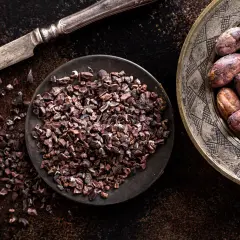 Un coltello d'argento accanto a una ciotola di **semi di cacao** tritati e un piatto decorato con semi di cacao interi.