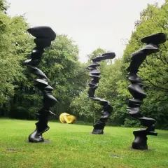 Drei schwarze, verdrehte Skulpturen stehen im **Skulpturenpark Wuppertal** auf einer grünen Wiese vor Bäumen. Eine gelbe Skulptur liegt im Hintergrund.