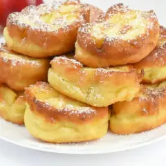 Puszyste racuchy na kefirze jak u babci, posypane cukrem pudrem. Obok leżą jabłka.