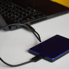 Un disque dur externe bleu est connecté à un ordinateur portable. Un guide pour comment choisir son disque dur externe.