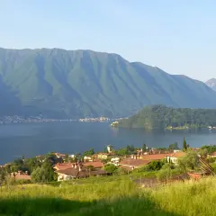 Villaggio sulle rive del lago più grande d'Europa, con montagne verdi sullo sfondo e un prato fiorito in primo piano.