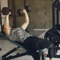 Mężczyzna wykonuje ćwiczenia na ławce, podnosząc hantle. Intensywny trening siłowy.