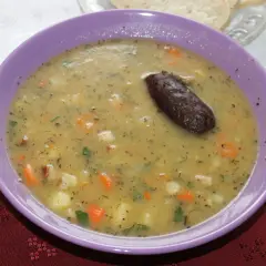 Gęsta zupa fasolowa z puszki, z kawałkami warzyw i ciemną kiełbaską, podana w fioletowej misce.