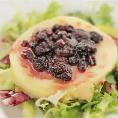 Provolone a la plancha cubierto con moras y salsa, servido sobre una cama de lechugas mixtas.