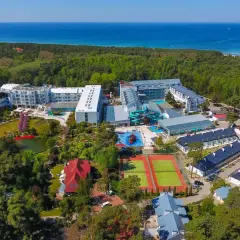 Widok z lotu ptaka na aquapark Pobierowo otoczony lasem, z widokiem na morze. Kompleks oferuje baseny, zjeżdżalnie i korty tenisowe.
