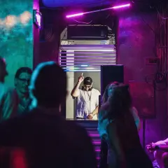 DJ w klubie, podniesiony palec, neonowe światła, różowy sober tekst.