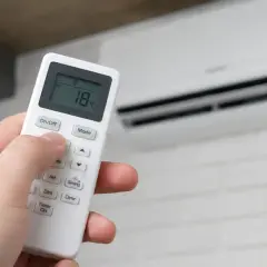 Mano ajustando el control remoto del aire acondicionado para un boost de aire fresco a 18°C.