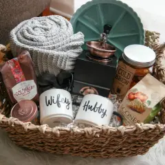 Cesta de mimbre con un kit para recién casados: tazas "Wifey" y "Hubby", café colombiano, scones, manta y más.