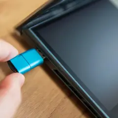 Dłoń podłącza niebieski pendrive do iPada. Dowiedz się, jak podłączyć pendrive do iPada, aby łatwo przenosić pliki.