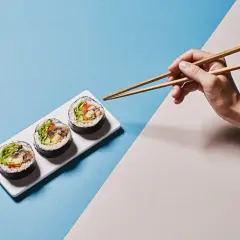 Dłoń z pałeczkami do sushi pokazuje, jak trzymać pałeczki do sushi, by złapać pyszne rolki.