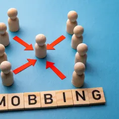 Drewniane ludziki otaczają jednego, a czerwone strzałki wskazują na niego. Słowo "MOBBING" na klockach.