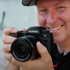 Uśmiechnięty mężczyzna trzyma aparat Fujifilm XH2S z obiektywem.