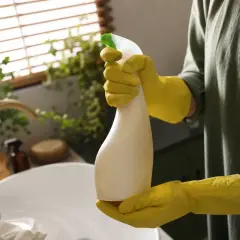 Gelbe Handschuhe halten eine Sprühflasche mit leicht vergilbtem Plastik.
