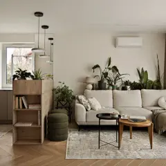 Jasna kuchnia z salonem, z zielonymi akcentami i mnóstwem roślin. Sofa w salonie, stoliki kawowe i regał z książkami.