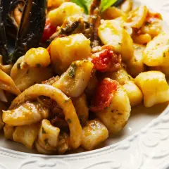 Gnocchi allo scoglio con cozze, calamari e pomodorini, un piatto ricco di sapori marini.
