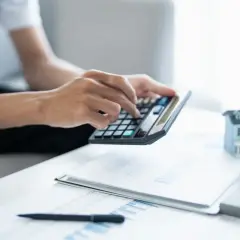 Man calculando la viabilidad hipoteca con calculadora, papeles y maqueta de casa.
