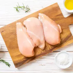 Tre petti di pollo crudi su tagliere di legno, con pepe, sale, olio e rosmarino. Ideale per un pasto leggero, scopri le calorie petto di pollo.