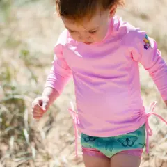 Małe dziecko w różowym stroju UV dla niemowląt z motylkami na kąpielówkach bawi się na plaży.