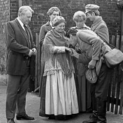 Scena z filmu "Antoni Lulek. Poglądy". Mężczyzna całuje dłoń starszej kobiecie, otoczeni przez innych ludzi.