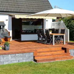 Eine schöne Holzterrasse mit Sitzmöbeln und Pflanzen, die zeigt, wie man eine Terrasse gestalten mit wenig Geld kann.
