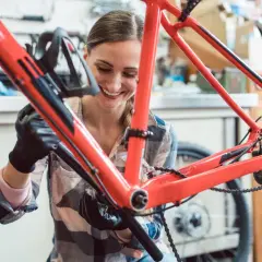 Uśmiechnięta kobieta w rękawiczkach dokonuje tuningu roweru, pracując przy czerwonej ramie.