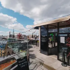 En takterrass med uteserveringar i Stockholm. Soliga moln på himlen, folk sitter vid borden och njuter av utsikten.
