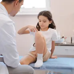 Dziewczynka wskazuje lekarzowi bolące kolano, być może to bóle wzrostowe u dzieci.