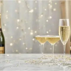 Kieliszki wypełnione musującym **brut champagne** i butelki na tle migoczących światełek. Idealny nastrój na świętowanie.