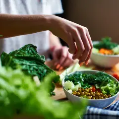 Mano che aggiunge erbe fresche a un'insalata colorata, ricca di fibre insolubili come piselli e verdure croccanti.