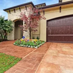 Stunning paver walkway ideas featuring a stamped concrete path leading to a home with a stone facade and a rich wooden garage door.