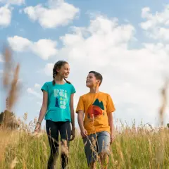 Two kids walk through a field of tall grass. A 50mm lens is good for capturing portraits like this, with a natural perspective and soft background blur.
