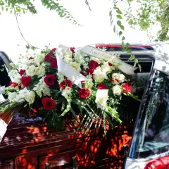 Wieniec z czerwonych i białych róż na trumnie, symbol ostatniego pożegnania. Wstęga z napisem "Your Family".