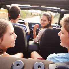 Famiglia in auto, divertiti con giochi da fare in macchina a voce. I bambini sorridono, la madre guarda indietro.