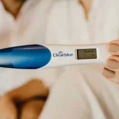 En hand håller ett digitalt graviditetstest som visar "Gravid 3+". Ett tidigt tecken på symtom på graviditet.