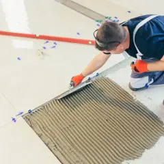 Fachowiec nakłada klej pod płytki. Zastanawiasz się, ile kosztuje fugowanie płytek?