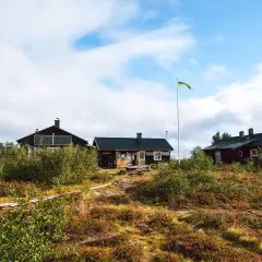 Mörka trähus med solpaneler och en svensk flagga som vajar vid ett vandrarhem i Dalarna.