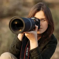 Kobieta z aparatem Canon EOS R7 uczy się, jak robić zdjęcia. Skupiona na kadrze, z obiektywem skierowanym w stronę widza.