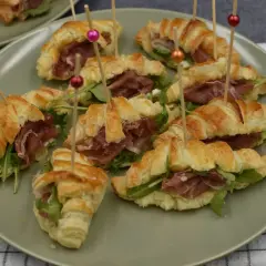 Na talerzu ułożono ile piec rogaliki z ciasta francuskiego, nadziane szynką parmeńską i rukolą.