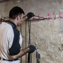 Mann führt eine Horizontalsperre im Mauerwerk durch. Bohrlöcher mit pinker Markierung und Kabel sind sichtbar.