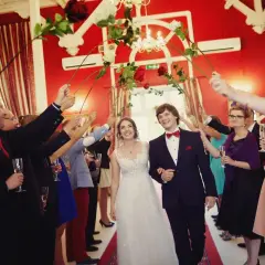 Para młoda przechodzi przez bramę weselną utworzoną przez gości z różami.