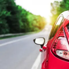 Auto rossa su strada panoramica, con sole che filtra tra gli alberi. Potrebbe indicare una **perdita potenza motore benzina** durante un viaggio.