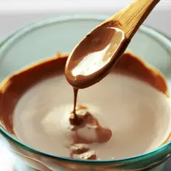 Geschmolzene Schokolade tropft von einem Holzlöffel in eine Glasschüssel. So schmelze ich Schokolade für süße Leckereien.