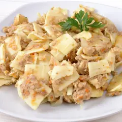 Łazanki z mięsem, kapustą i pieczarkami, udekorowane natką pietruszki, na białym talerzu.