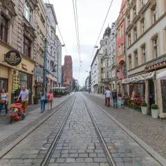 Spacer po starówce Wrocław, ulica z torami tramwajowymi i kamienicami. Rodzina z wózkiem spaceruje po bruku.