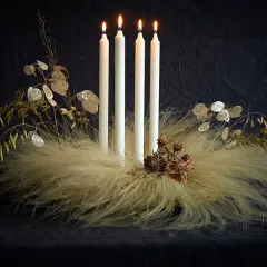 Ausgefallener Adventskranz Trend: Vier weiße Kerzen auf einem Bett aus Federn und Gräsern, geschmückt mit Lunaria und Zapfen.