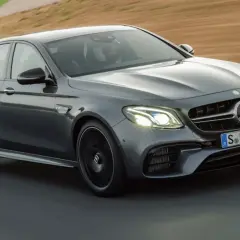 Szary Mercedes-Benz E63 AMG na torze wyścigowym, z kierowcą w kasku za kierownicą.