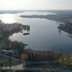 Jesioro Kałębie w jesiennej odsłonie, z widokiem na spokojną taflę wody, otoczoną drzewami w barwach złota i czerwieni.