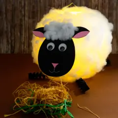 Ein leuchtendes Schaf, gebastelt aus einem Luftballon, mit Watte als Wolle und Papier für Kopf und Ohren.