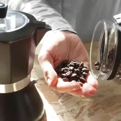 Czarna kawiarka i ręka z ziarnami kawy wysypującymi się ze słoika. Idealna kawa w lodówce czeka na zaparzenie.