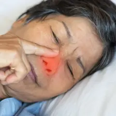 Una persona mayor con un dedo en la nariz, con una zona roja que indica dolor o irritación. ¿Qué pasa si te comes los mocos?